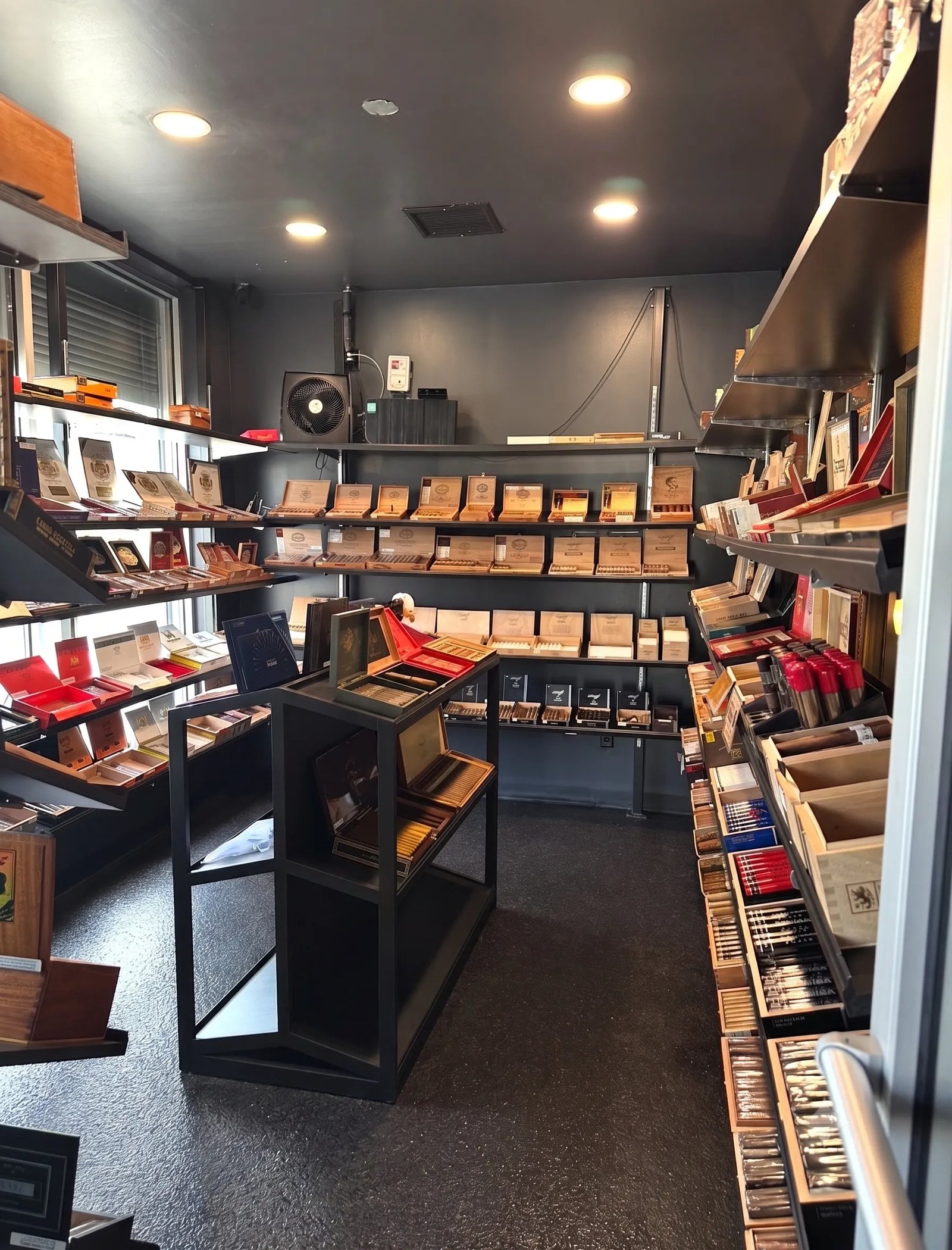 Walk-in humidor at Palomino Cigar Lounge with shelves of open cigar boxes on dark walls