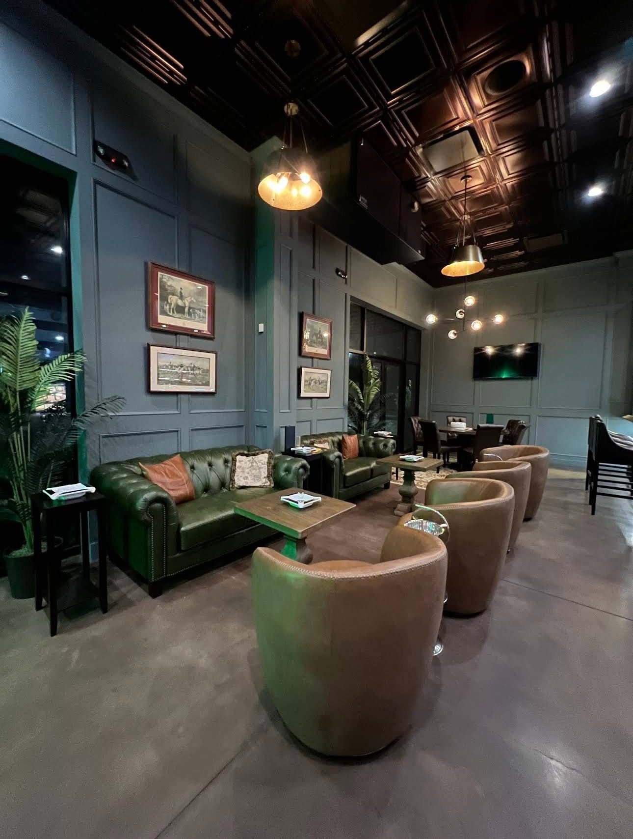 Lounge at The Royale with green tufted leather sofas, leather tub chairs, paneled walls, and framed equestrian prints