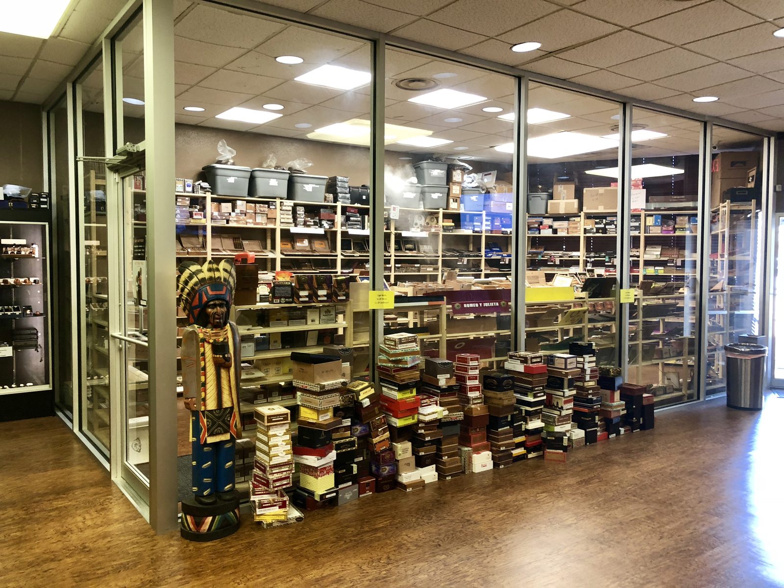 Glass walk-in humidor at The Tobacco Pouch with shelves and stacks of cigar boxes